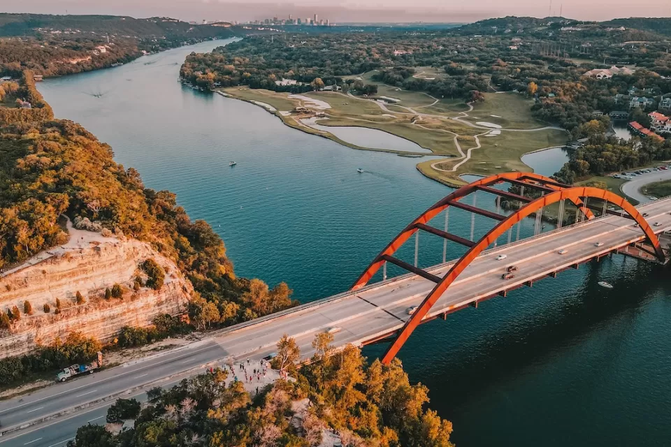 Aerial view of Pennybacker Bridge in Austin, Texas. Bridge over river with orange arches and downtown Austin visible in far background.